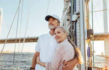 Affectionate senior couple hugging together and looking into the distance while standing on a yacht