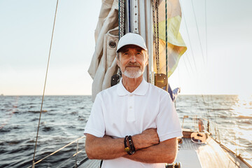 Portrait of a mature confident captain standing on his yacht at mast and looking at camera