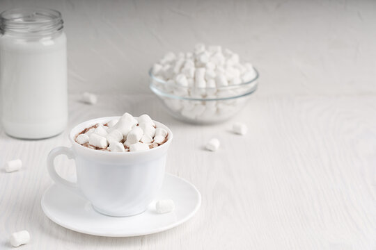 White cup full of homemade caco drink usually cooked at hold winter vacations served on plate with marshmallows and jar of milk on wooden background at kitchen. Image with copy space, horizontal