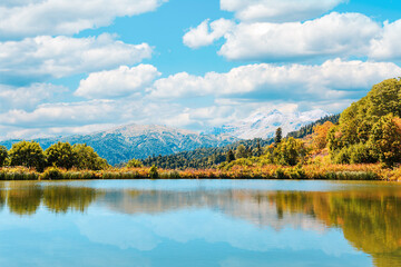 Autumn landscape. View of the lake and the autumn forest. Blue sky with clouds