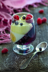 glass jar with dessert (panna cotta, jelly, mousse, pudding) with bilberry and banana layers on wooden rustic table
