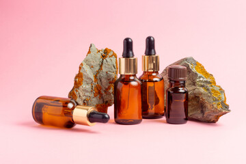 An amber bottle for essential oils and cosmetics stands next to the stone. Glass bottle on a pink...