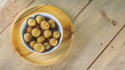 Overhead view of longan fruits on white bowl- wooden background