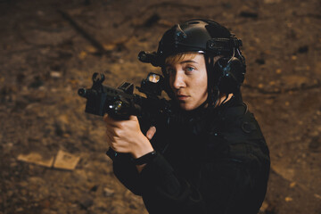 Young woman soldier in black uniform aiming up with an assault rifle.
