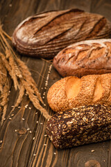 selective focus of fresh baked bread loaves with spikelets on wooden surface