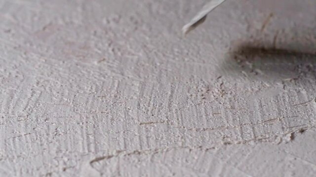 with a spatula, apply white granular plaster on a horizontal surface, closeup