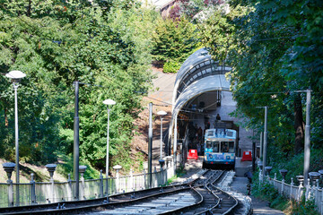 A blue and white cable funicular picks up passengers at the lower station, surrounded by a summer...