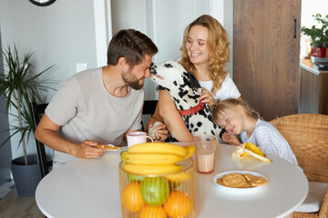 young caucasian family have breakfast together, in the kitchen. they have friendly dog pet, in love.