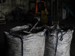 Fototapeta na wymiar Cloth fleecy white agricultural bags with coals, inside a shovel, coals factory