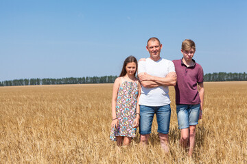 Naklejka na ściany i meble Dad with pre-teen son and daughter, full length portrait, Caucasian single father with two kids standing on wheat field at summer, copy space