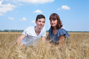 Adult mother with her teenage son sitting in yellow wheat field, two Caucasian people
