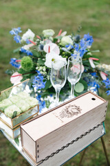 Close up of shelf with wedding glasses, floral composition of white, blue flowers outdoors. Beautiful decorated furniture for ceremony. Traditional elements of wedding celebration. Concept of beauty.