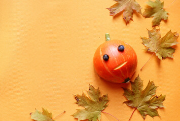 Pumpkin man with scattered maple leaves on an orange background, top view concept of a rich autumn...