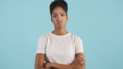 Portrait of frustrated african american girl holding arms crossed and sadly looking in camera over blue background