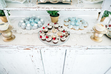 Front view of delicious sweet cupcakes, mousse desserts on wedding candy bar. Tasty patisserie on white table. All inclusive menu. Luxury birthday celebration nutrition. Concept of calorie and food.