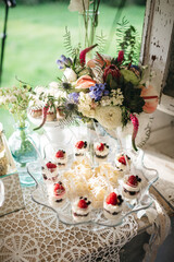 Top view of beautiful floral composition and delicious cupcakes on wedding sweet bar. Tasty desserts decorated with strawberry. Luxury birthday catering. Concept of homemade patisserie, yummy food.