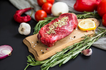 Raw beef steak on a cutting board with spices. Creative atmospheric decoration.