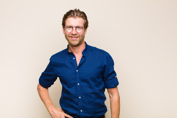 blonde adult caucasic man smiling happily with a hand on hip and confident, positive, proud and...