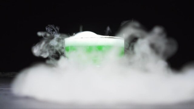 Magic potion is brewed in a glass bowl on a black background. Close-up.