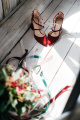 Top view of red footwear prepared for unusual wedding ceremony lying on floor in sunlight rays. Morning preparation for wedding celebration, bridal shoes fashion. Concept of details on wedding day.