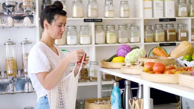 Woman is shopping organic fruits and vegetables in zero waste eco shop with mesh bag. Sustainable plastic free lifestyle