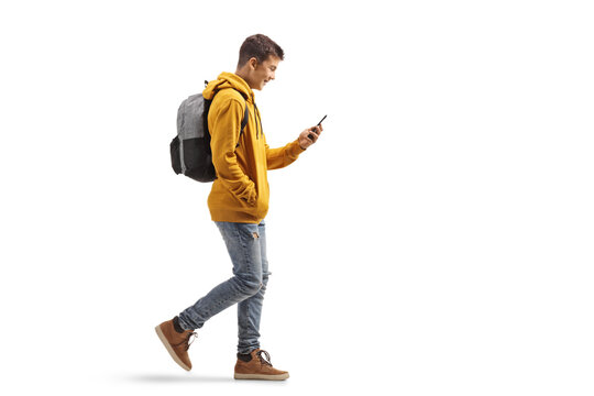 Full Length Profile Shot Of A Male Teenage Student Walking And Looking At A Mobile Phone