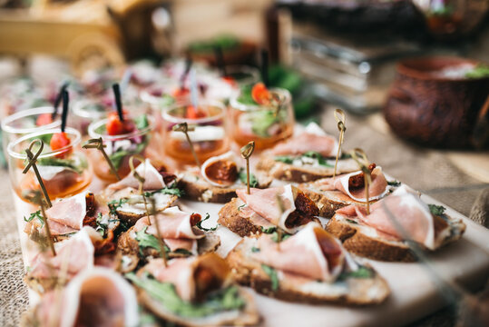 Close up of delicious appetizers on luxury wedding snack bar. Table catering with canapes with meat and arugula on baguette. Cooking simple french recipes. Concept of beautiful nutrition, calories.