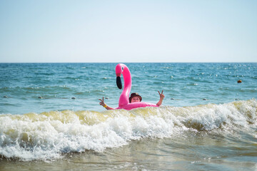 A girl in a swimsuit swims in the sea on an inflatable pink flamingo circle. The waves in the sea.