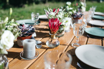 Close up of open air table serving with beautiful fresh flower bouquet and candles, blue plates on backyard. Preparing for amazing dinner with family on sunny day. Concept of summer time and beauty.