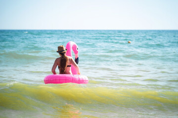 A girl swims in the sea on an inflatable pink Flamingo. Swimming on the waves. Black sea coast.