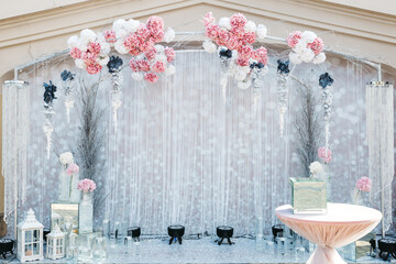 Full view of beautiful tender dim blue wedding photo zone decorated with white and pink flowers. Restaurant interior floral decoration. Charming florist job. Archway for ceremony. Concept of beauty.