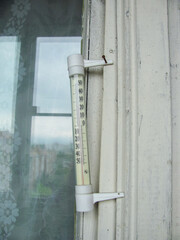 an atmospheric thermometer hangs on the window on the balcony