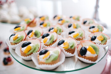 Close up of yummy creamy cupcakes on tray on sweet birthday bar. Delicious bakery decorated with fresh fruits, wedding celebration catering on bakery buffet. Concept of healthy desserts and dieting.