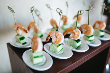 Close up of appetizer of cooked shrimp and fresh cucumber on tiny white glassware. Delicious food on wedding snack bar. All inclusive. Restaurant daily specials. Concept of luxury life and tasty food.