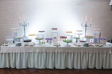 View from distance of white buffet table with delicious colorful desserts. Wedding catering on...