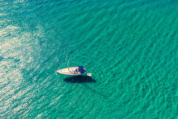 Yacht anchoring in crystal clear turquoise water in front of the tropical island, alternative lifestyle, living on a boat. Aerial view of yacht at anchor on turquoise water, showing luxury, wealth.