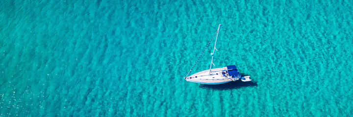Aerial view of anchored sailing yacht in emerald sea. Aerial view of a boat. Outdoor water sports,...