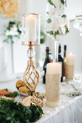 Front view of burning candles in elegant candlestick on decorated with fresh floral composition table in luxury restaurant. Charming interior element for wedding ceremony. Concept of stylish details.