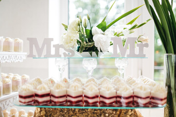 Close up of delicious pana cotta with floral composition made of white eustomas and tablets of mr and mrs. Beautiful party catering with sweet yummy dessert. Concept of cooking and restaurant serving.