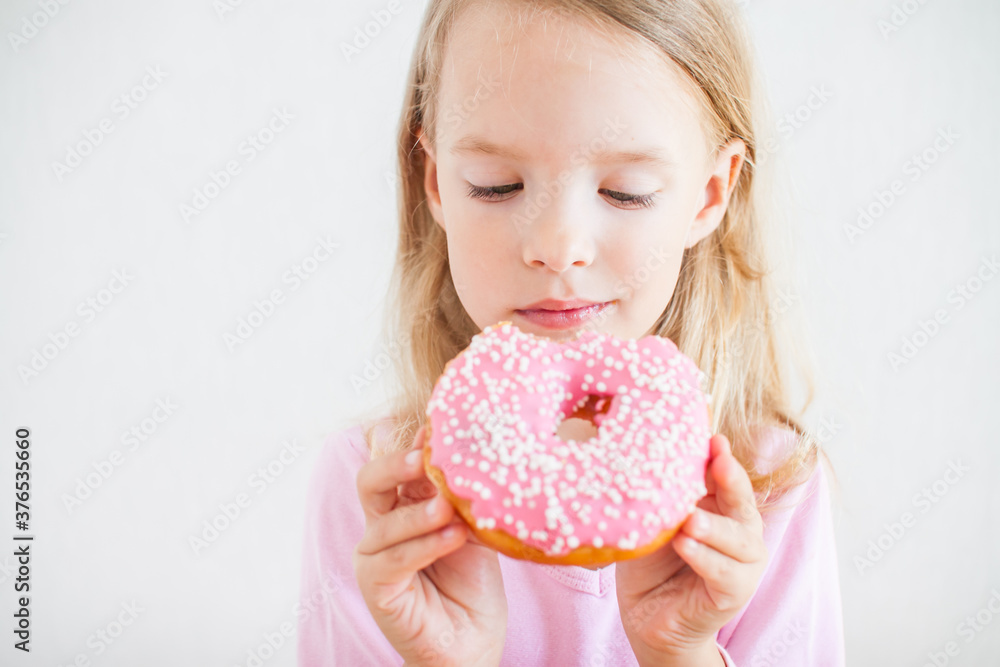 Wall mural little happy girl with blond hair playing and tasting donuts with pink icing at hanukkah celebration