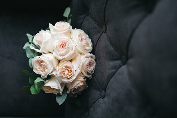 Front view of beautiful wedding bouquet for bride made of pale orange roses on grey sofa. Lying pretty bouquet, preparing for romantic date, anniversary floral surprise. Concept of tender love gifts.