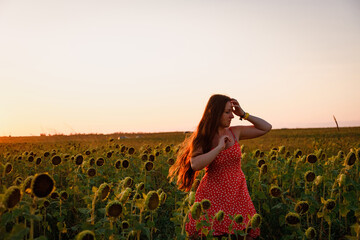 a young beautiful girl in a red dress with white polka dots walks in a sunflower field. sunset in the field.