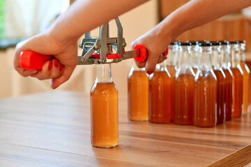 Using hand capper for home brewing. Background of brown bottles with homemade liquor or alcohol. Selective focus.