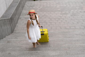 Beautiful tourist girl travels. Pulls a heavy, large yellow suitcase up the steps.
