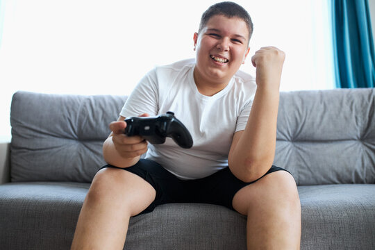 fat boy happy for winning the video game, sits on sofa in living room, relax, spare time at home