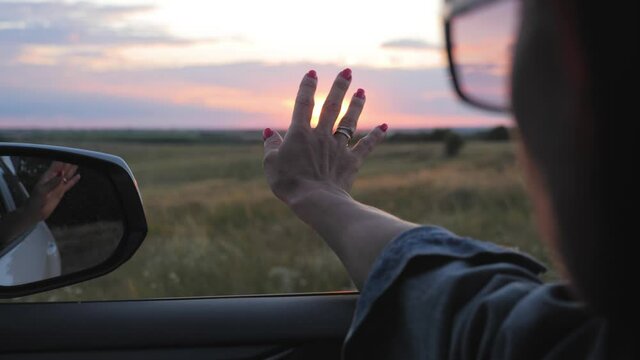 Beautiful girl holding arm out of car window friend enjoying road at sun.