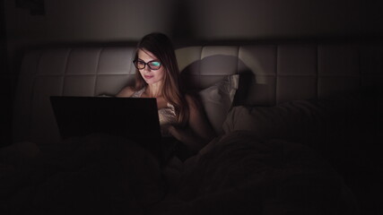 woman in glasses works on a laptop in the dark. portrait of a girl spending time at the computer late in the evening
