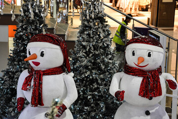 There are two snowmen in the mall next to the trees. Christmas background with snowmen and fir trees in the trading floor.
