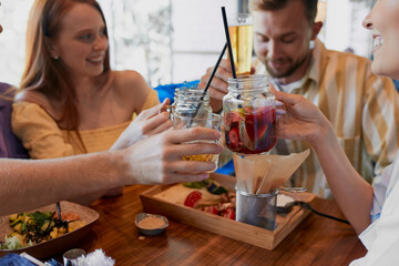 group of young people clink glasses with beverages in restaurant or bar, have a great time at weekends, some rest
