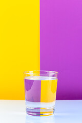 Optical illusion with glass of water and colorful paper, yellow and violet background, vertical, copy  space